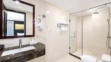 A modern bathroom with a marble sink, a large mirror, a hairdryer, and a glass-enclosed shower.