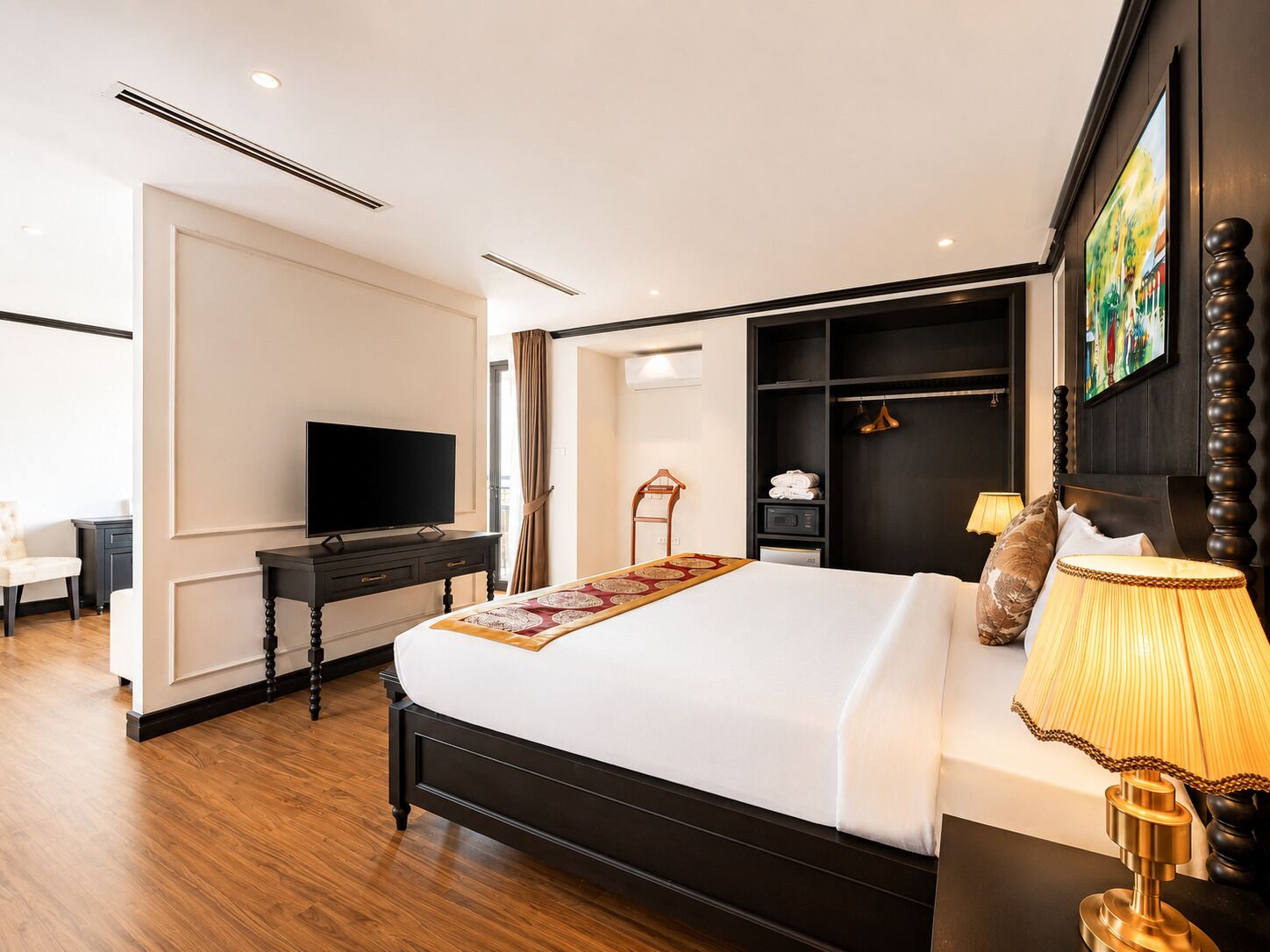 Habitación de hotel con cama, escritorio con televisor, armario y un cuadro en la pared.
