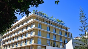 Un hotel de varios pisos con balcones, un cielo azul despejado y algo de vegetación.