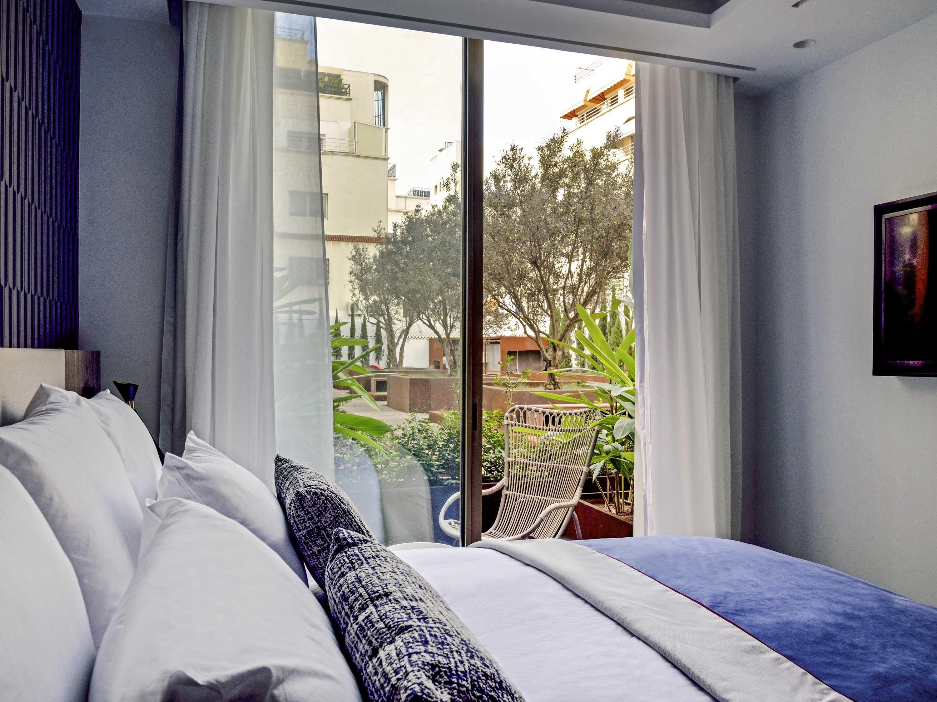 Une chambre avec un grand lit, une vue sur l’extérieur grâce à une porte coulissante, et une chaise à l’extérieur.