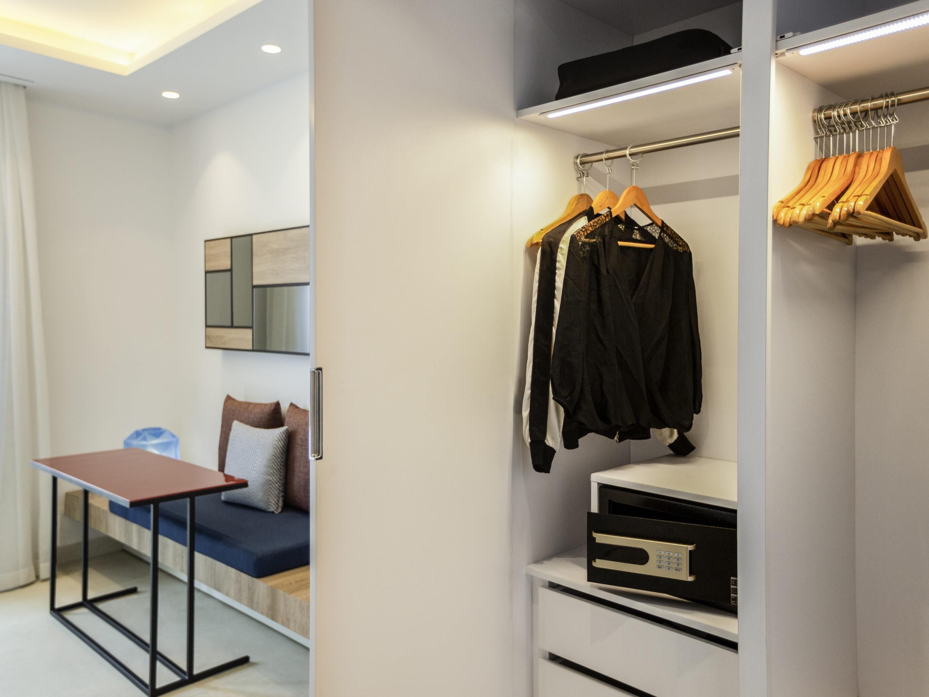 Une chambre à coucher moderne, avec un lit, une table de chevet et un dressing où sont rangés des vêtements sur des cintres et une étagère.