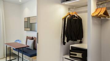 Une chambre à coucher moderne, avec un lit, une table de chevet et un dressing où sont rangés des vêtements sur des cintres et une étagère.