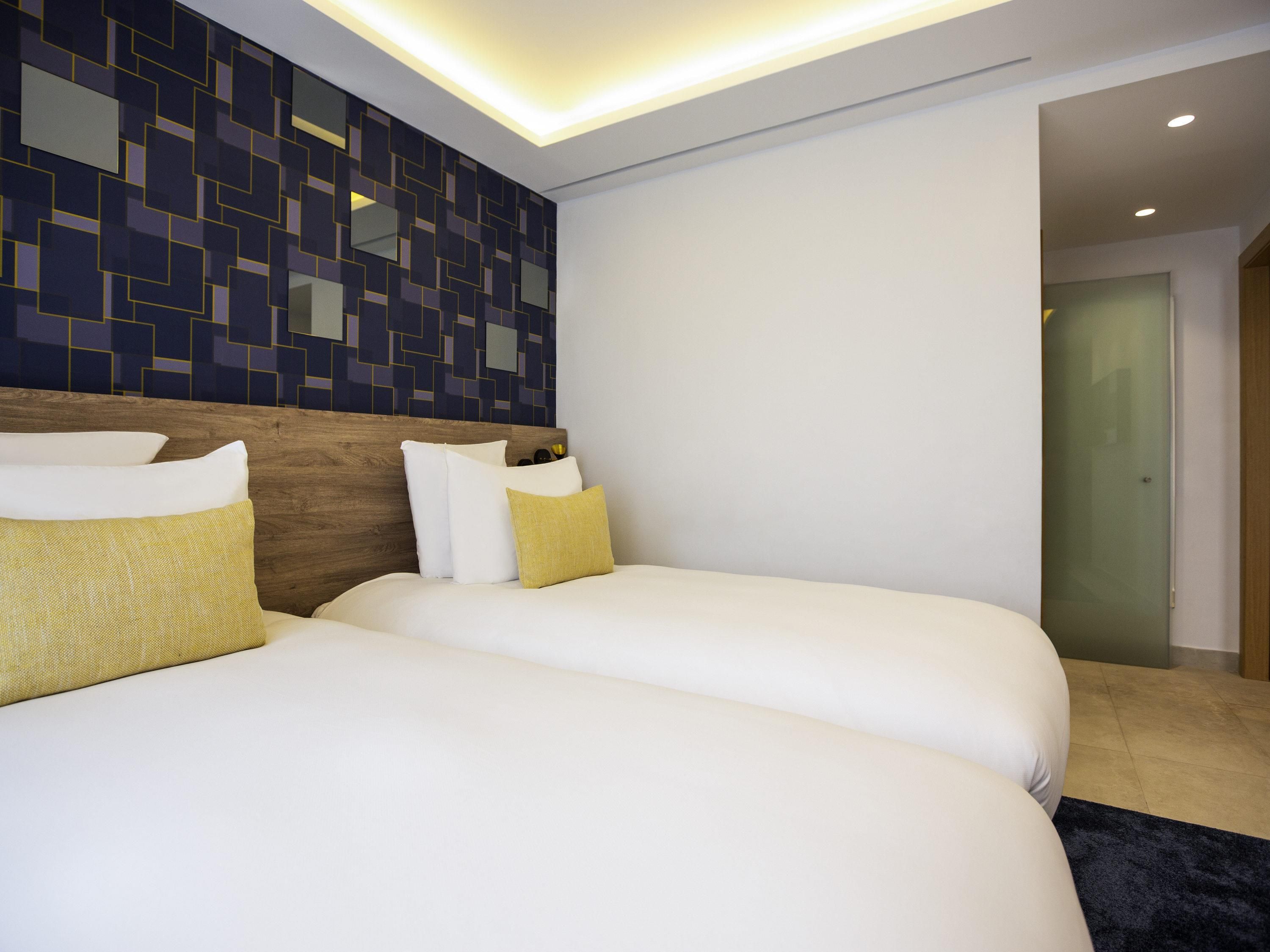 Una habitación de hotel con dos camas, un cabecero de madera y una pared con un diseño geométrico.