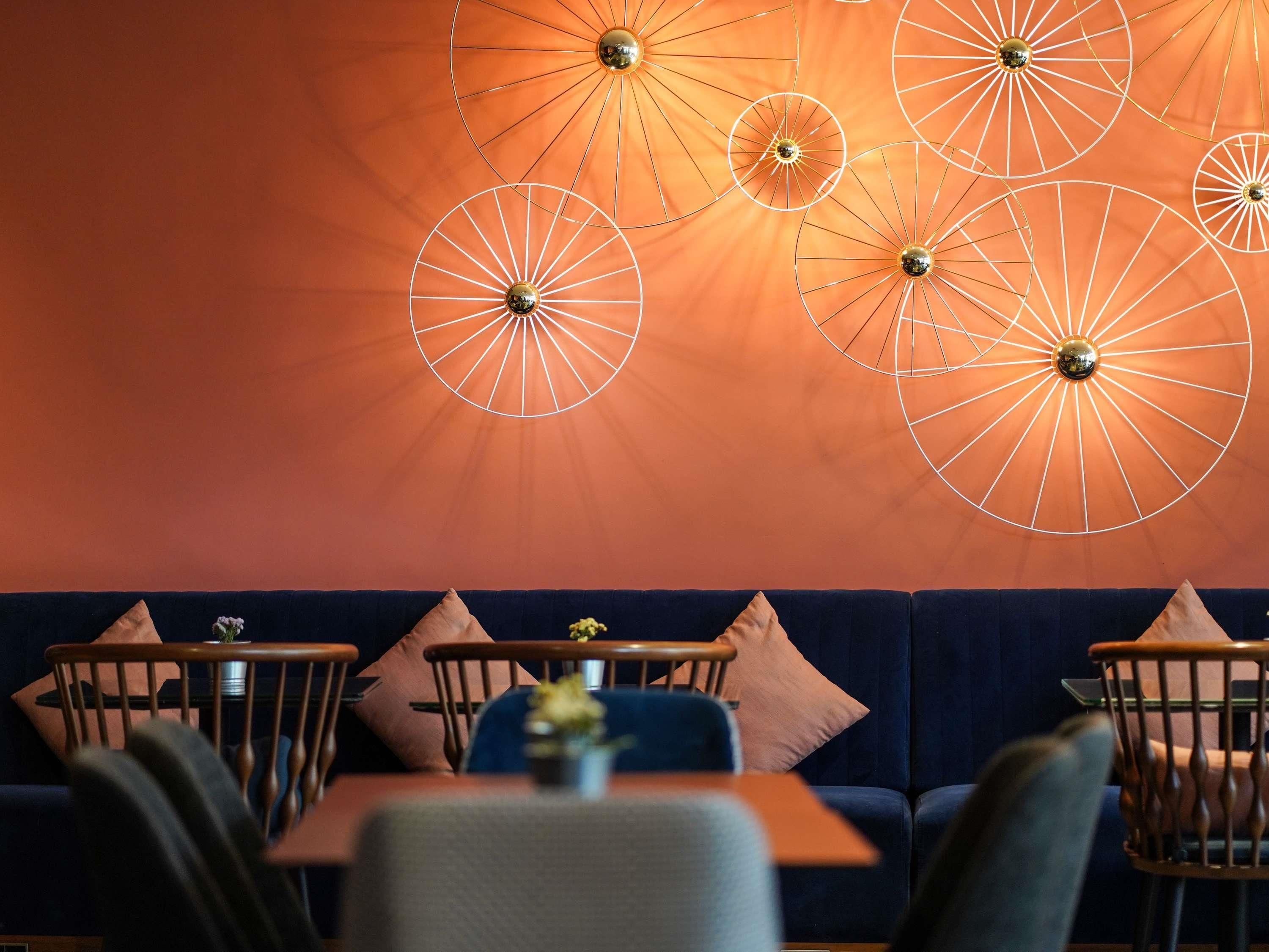 Eine Sitzecke mit einem dunkelblauen Sofa und Holzstühlen, einem Tisch mit Blumenvase sowie runden Wandleuchten.