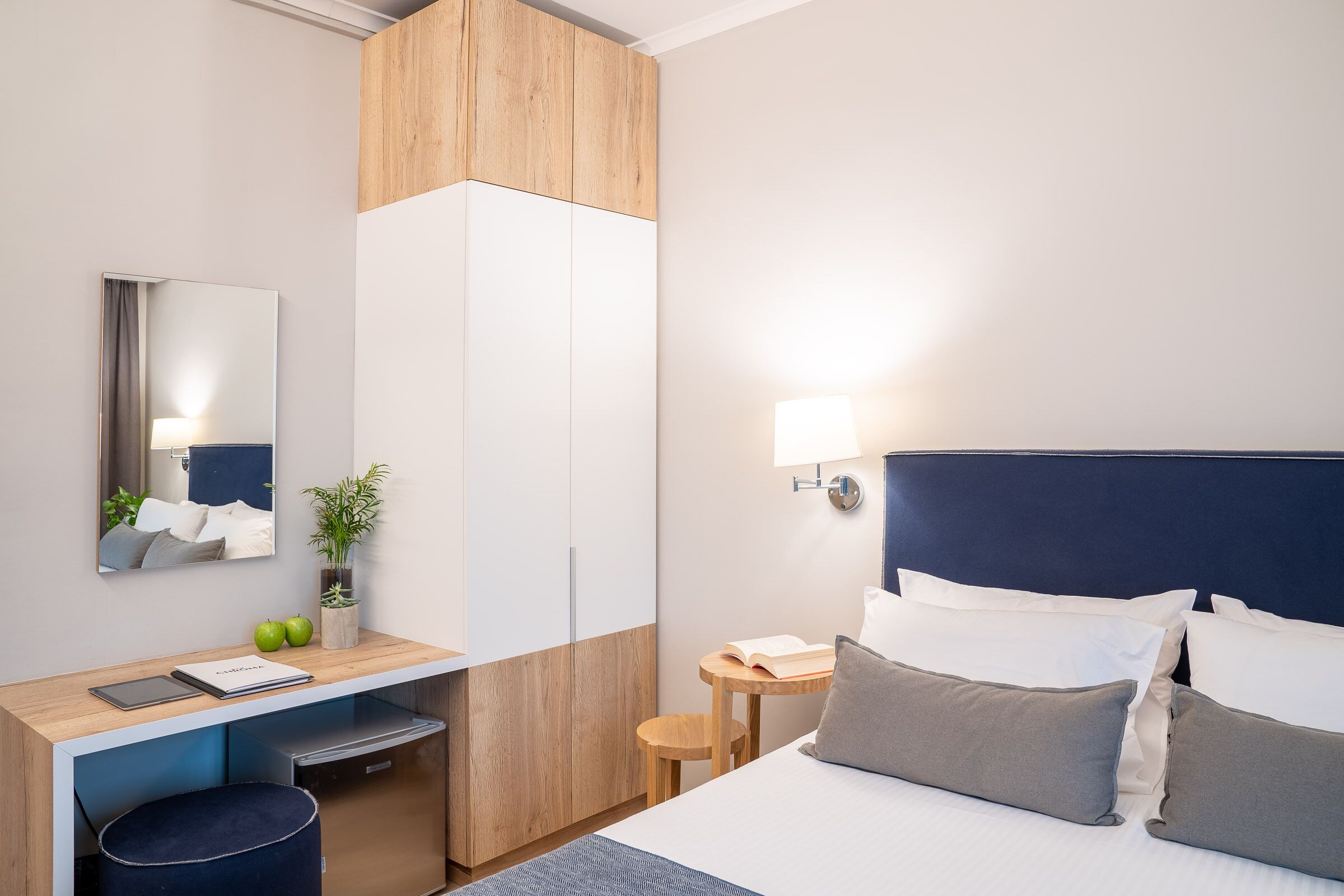 A hotel room with a bed, bedside table, desk, chair, and a mirror.