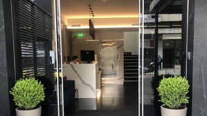 The entrance to Chroma Fashion Hotels with a modern design, featuring a reception desk, a staircase, and potted plants. - Chroma Fashion Rooms & Apartments (Chalandri)