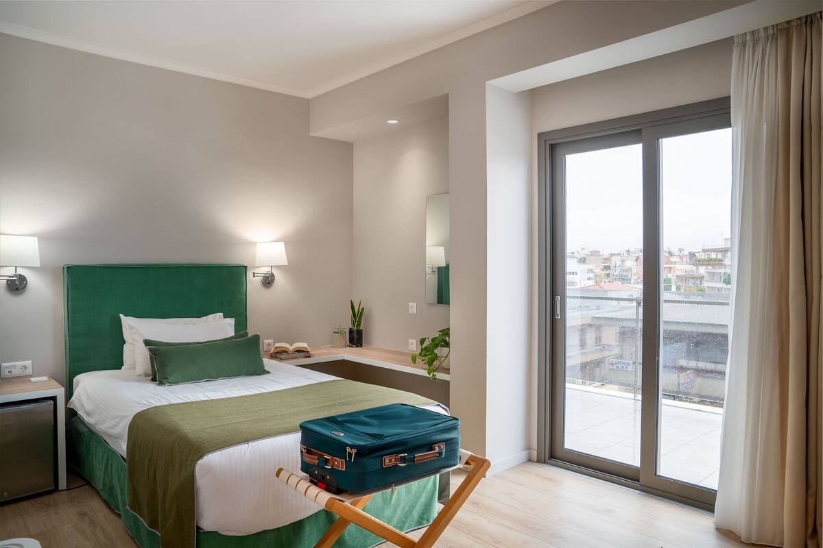 A hotel room with a bed, bedside table, lamp, and a suitcase on a trolley.