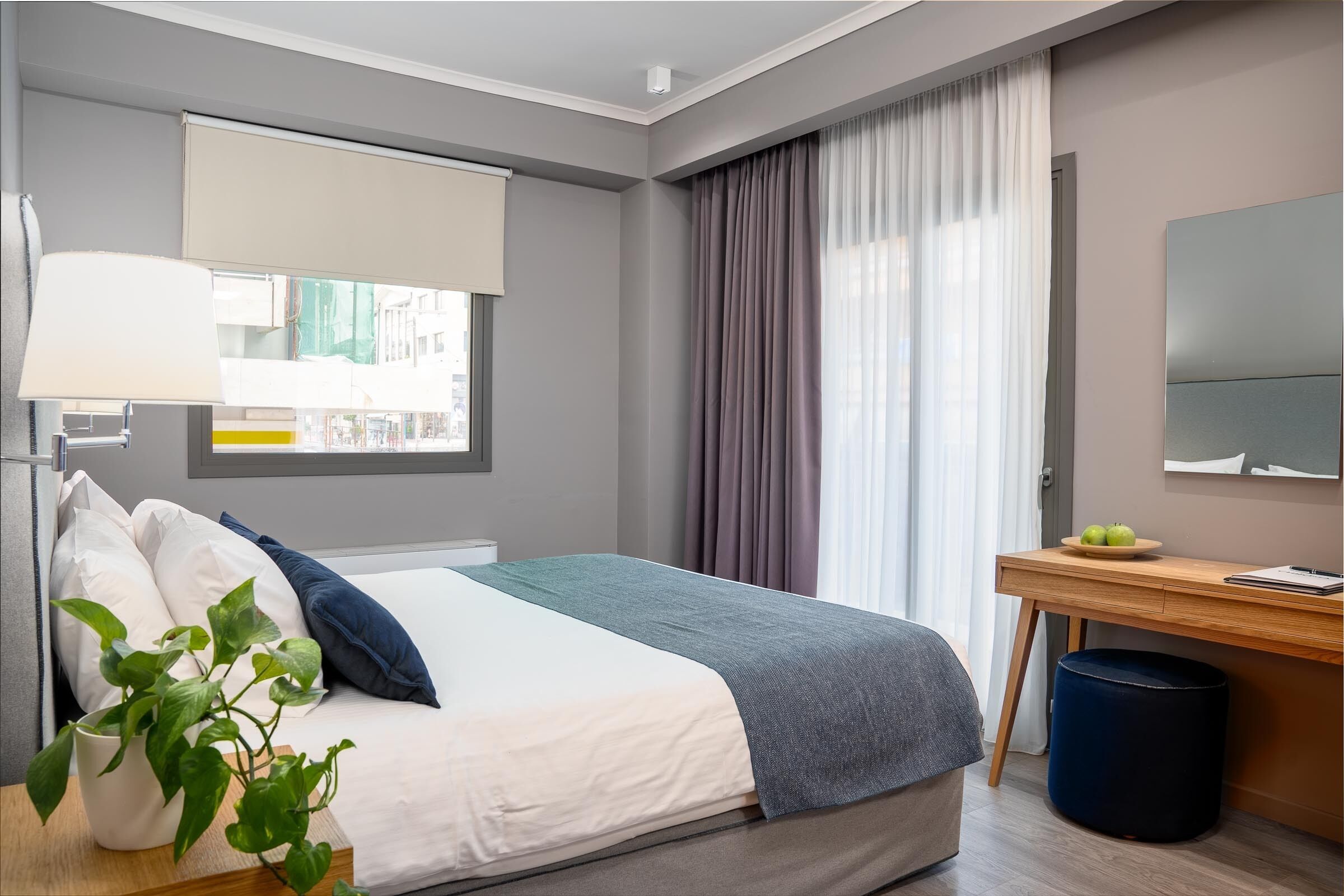 Una habitación de hotel moderna con cama, escritorio, lámpara y ventana con cortinas.