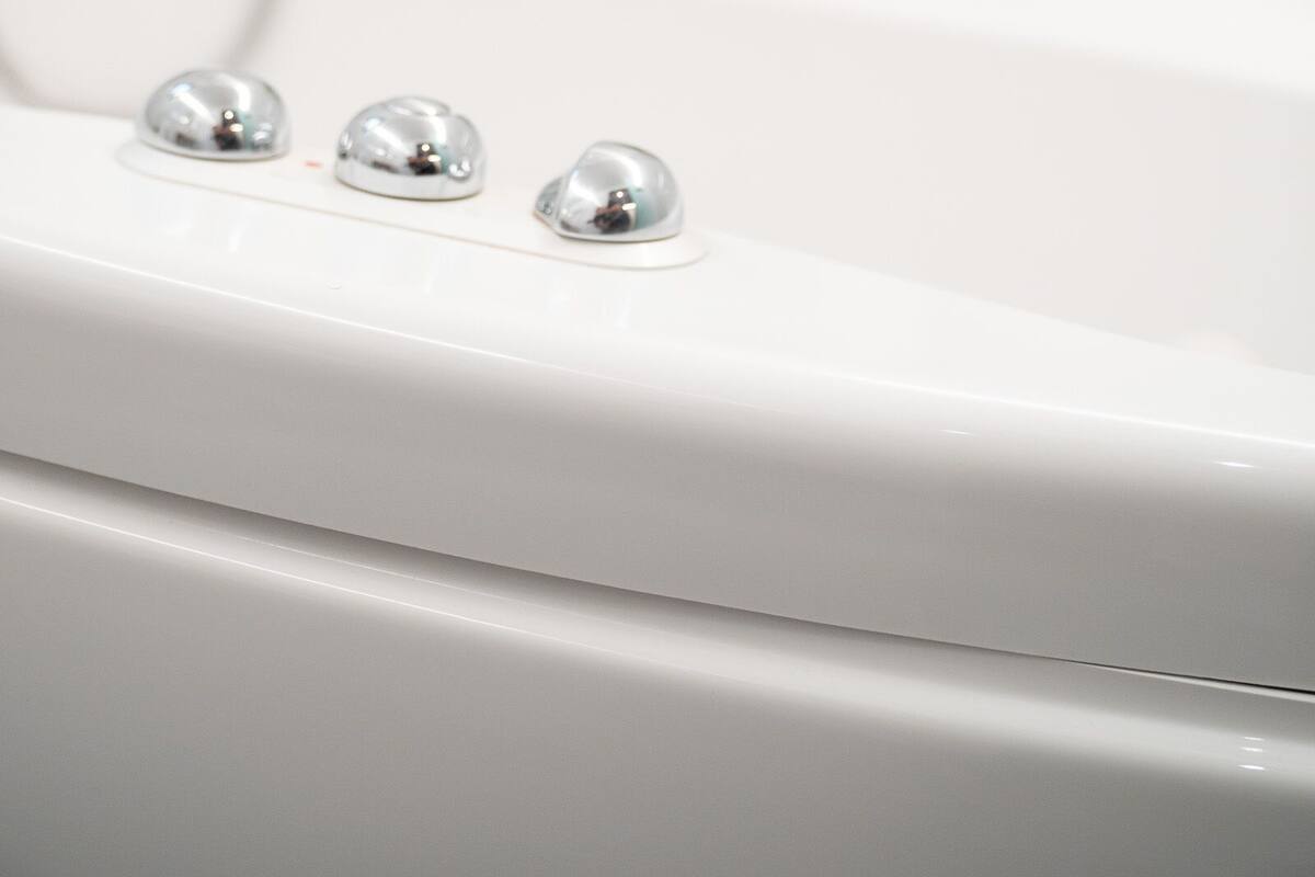 A white bathtub with three chrome knobs and a potted plant on a shelf in the background.