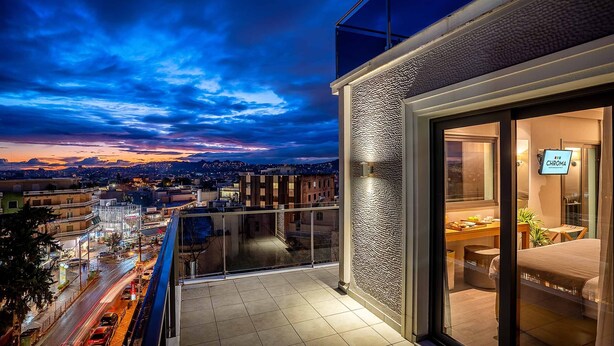 A modern hotel room with a balcony overlooking a cityscape at dusk. - Chroma Fashion Rooms & Apartments (Chalandri)