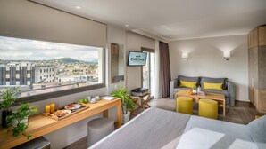 A modern hotel room with a city view, a desk with breakfast items, a sofa, and a television. - Chroma Fashion Rooms & Apartments (Chalandri)