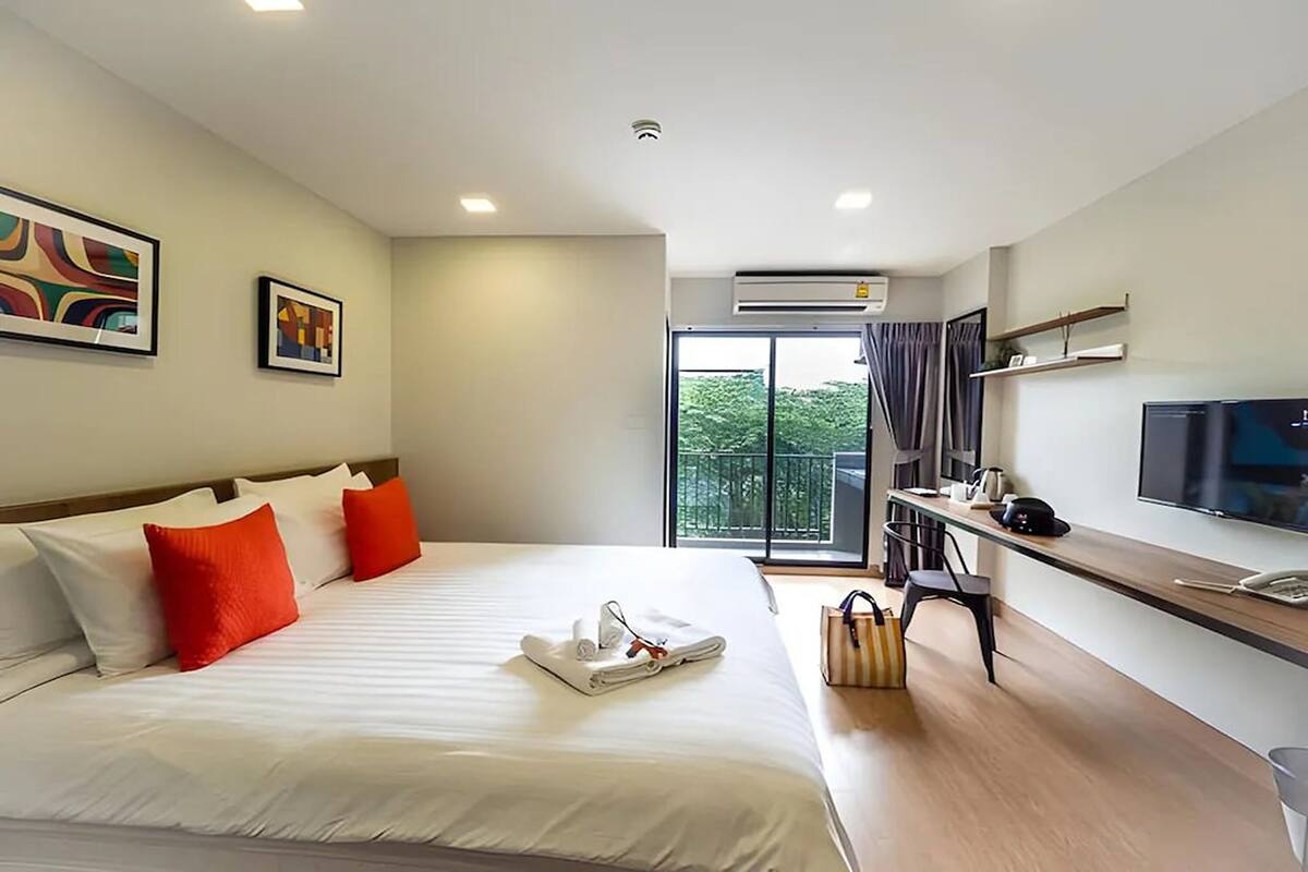 Habitación de hotel con una cama, un escritorio con computadora, televisión y balcón con vistas.