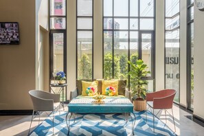 A modern room with large windows, a sofa with colorful pillows, a small table with a plant, and two chairs. - Casaluxe Hotel Ratchada (Bangkok)