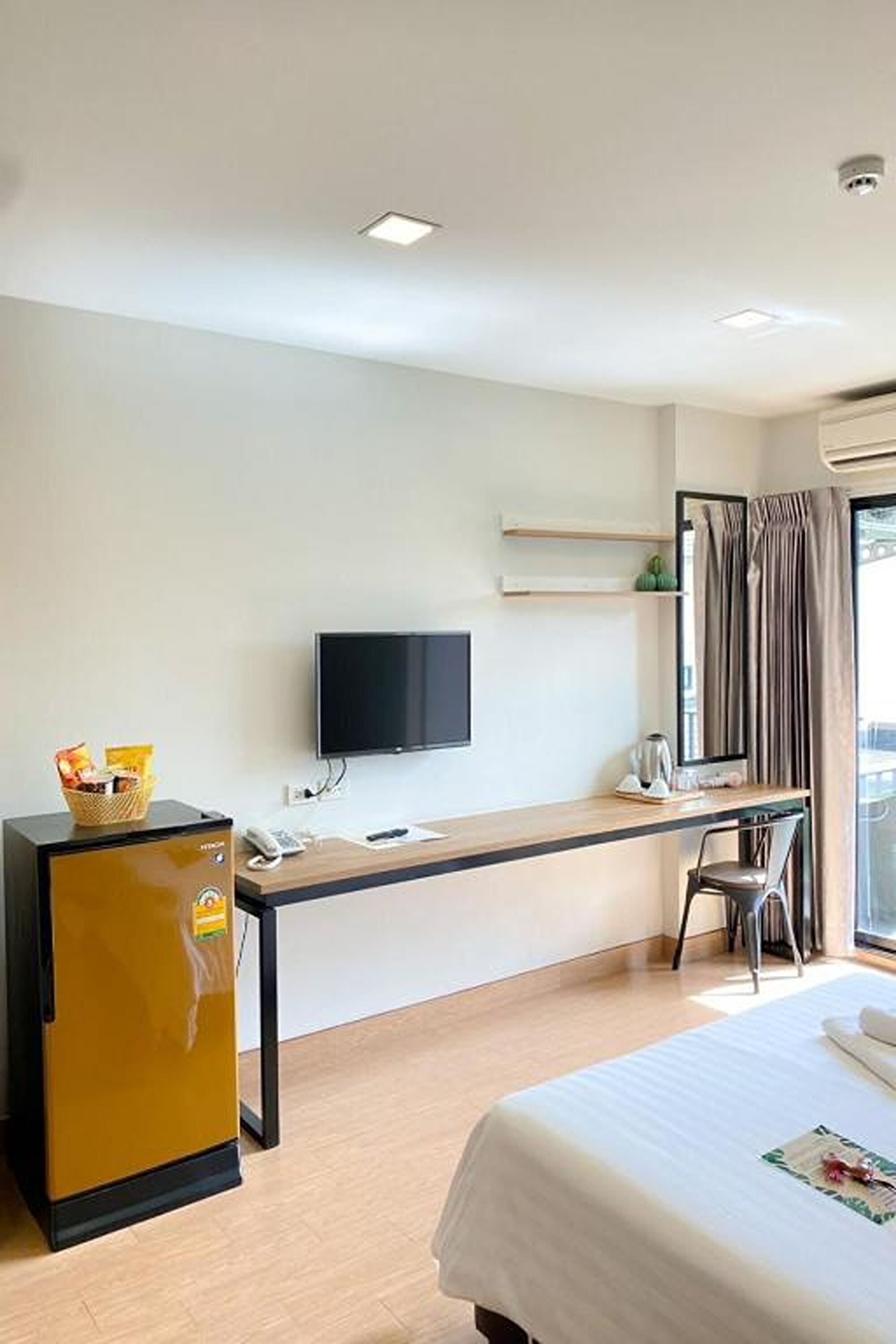 Una camera d'albergo con un letto, una scrivania con un computer e una televisione a schermo piatto, un piccolo frigorifero e una finestra con tende.