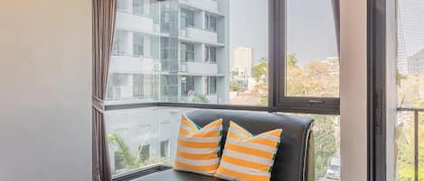 A modern apartment with a large window, a black leather sofa with striped cushions, and a view of a cityscape.
