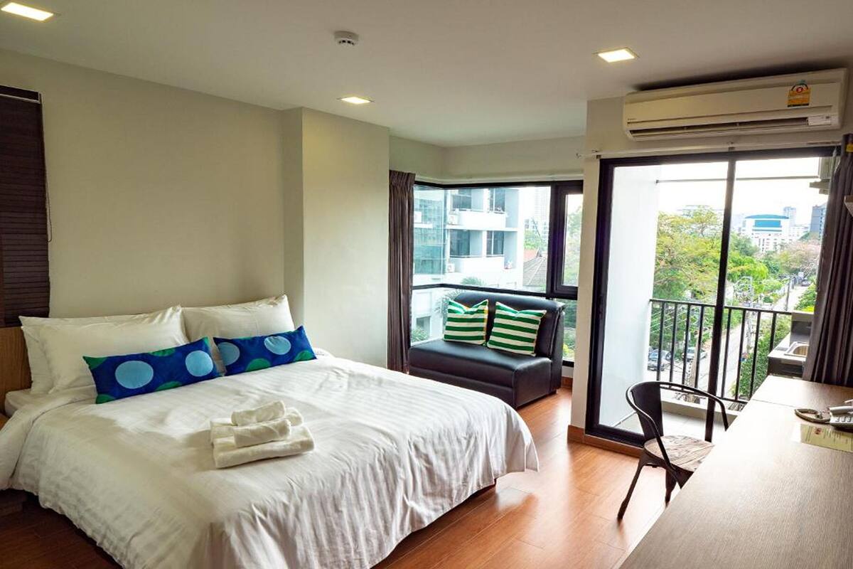 Habitación de hotel con una cama grande, un sofá pequeño, un balcón con vistas y un aire acondicionado.