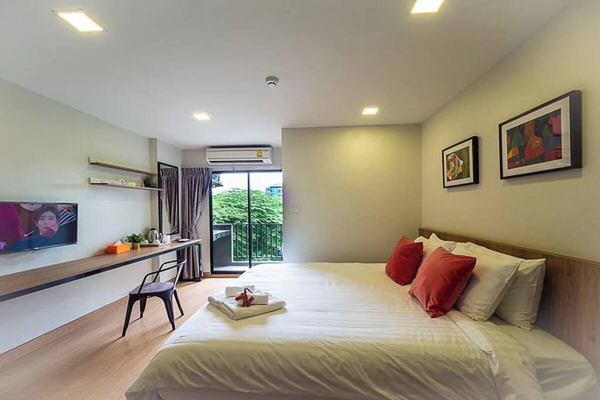 Habitación de hotel con cama, escritorio, silla, televisor y balcón con vistas.