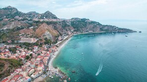 Uma vila costeira com edifícios ao longo da costa, barcos na água e um relevo acidentado ao fundo.
