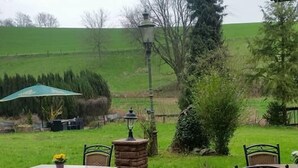 An outdoor patio with tables and chairs, a stone lantern, and a view of a green field. - Der Watzenhof (Hemsbach)