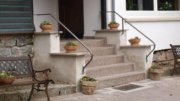 A building with a stone facade, a wooden bench, and a staircase leading to a door. - Der Watzenhof (Hemsbach)
