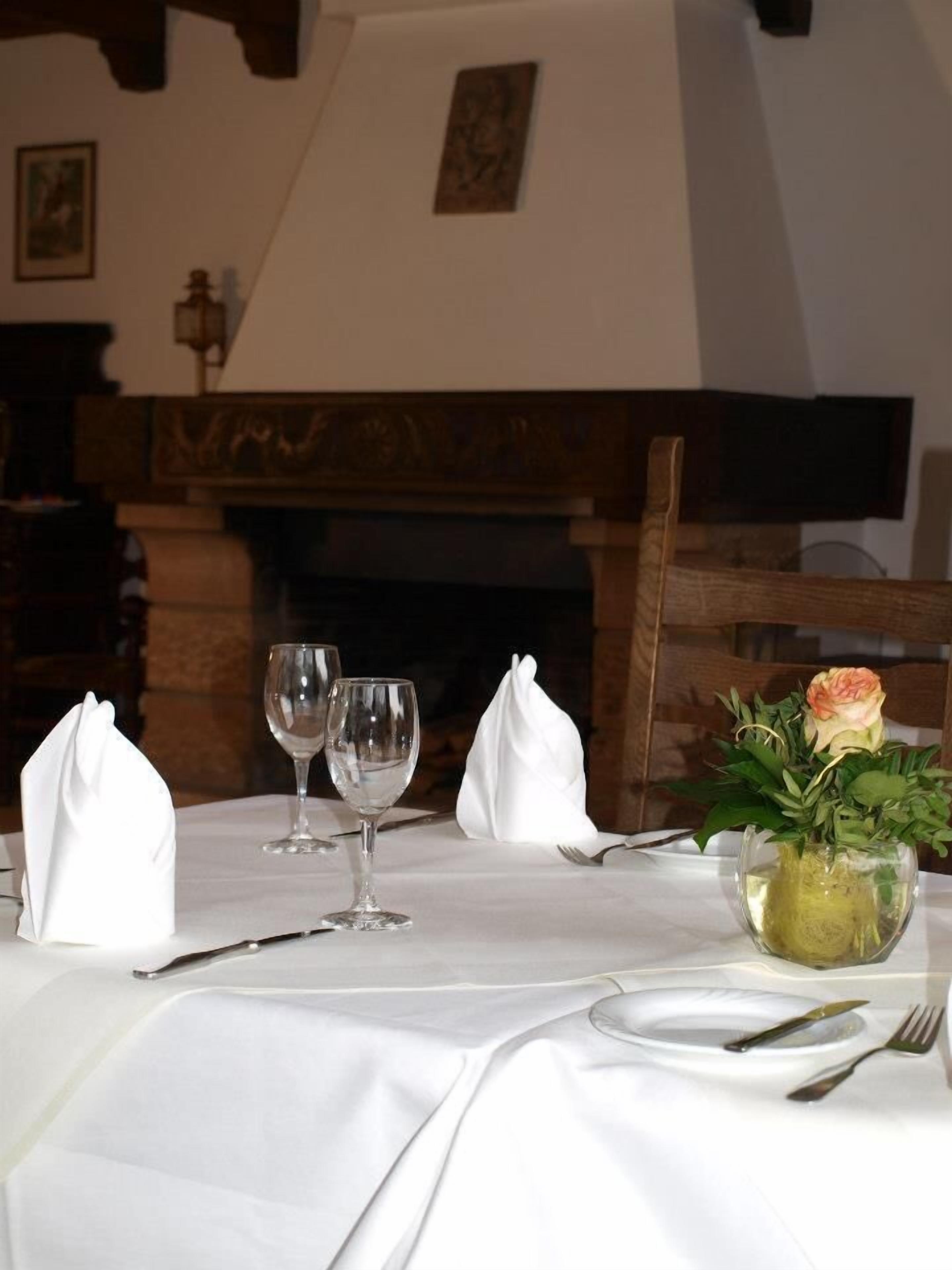 A dining table set with white tablecloth, wine glasses, plates, and cutlery. There is a vase with a flower on the table.