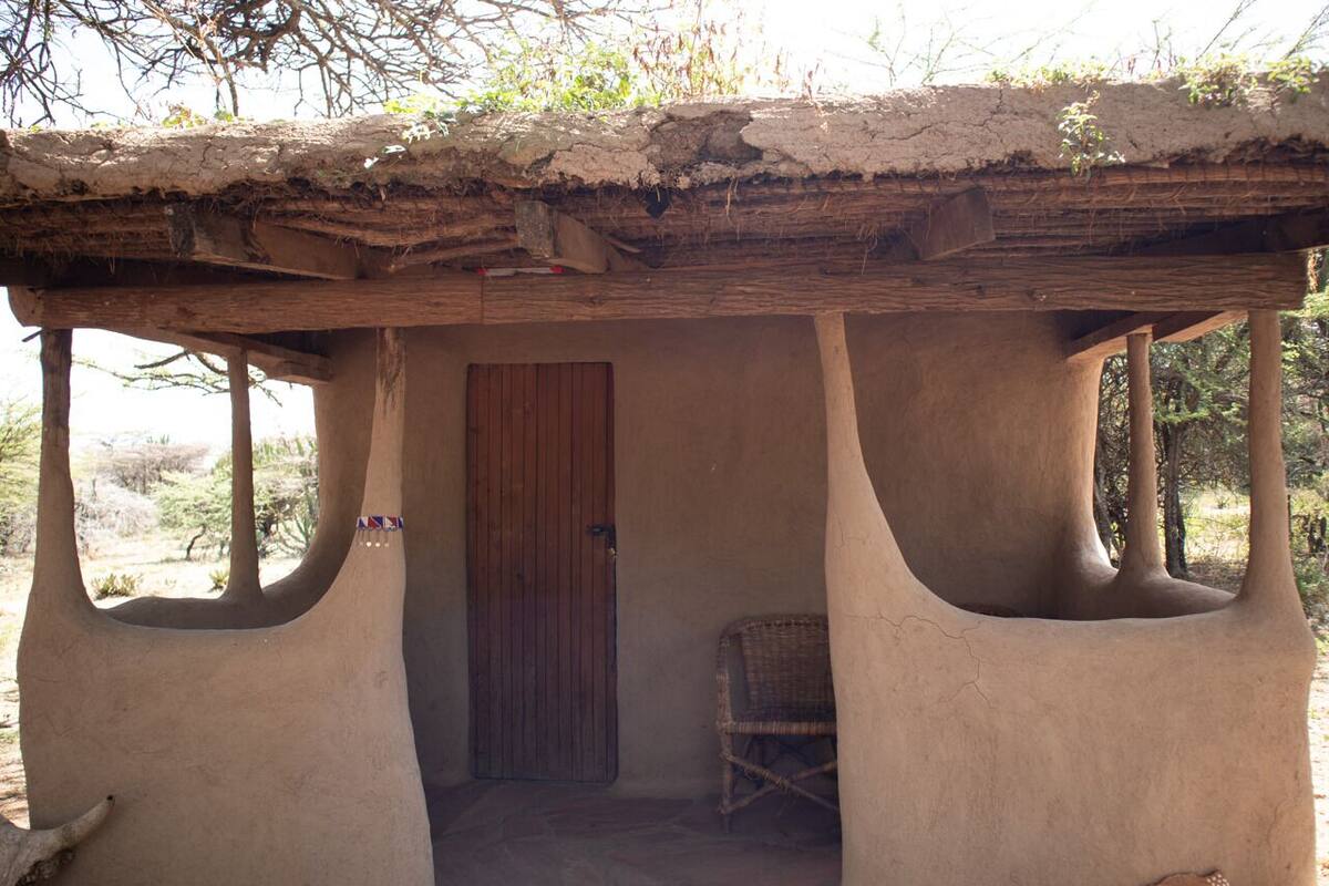 A traditional mud hut with a wooden door and a woven chair inside.