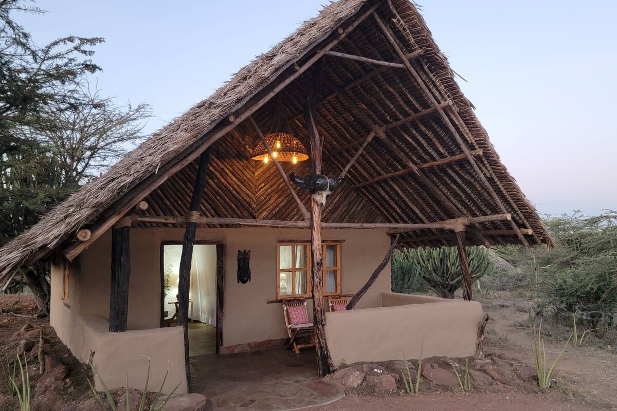 A thatched-roof hut with a simple interior, a wooden chair, and a hanging light fixture.