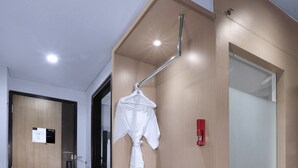 Habitación de hotel con puerta de madera, un escritorio pequeño con teléfono, una prenda colgada y un detector de incendios.