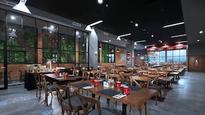Un comedor espacioso con varias mesas y sillas, amplias ventanas con vistas a zonas verdes y un diseño moderno de techo.