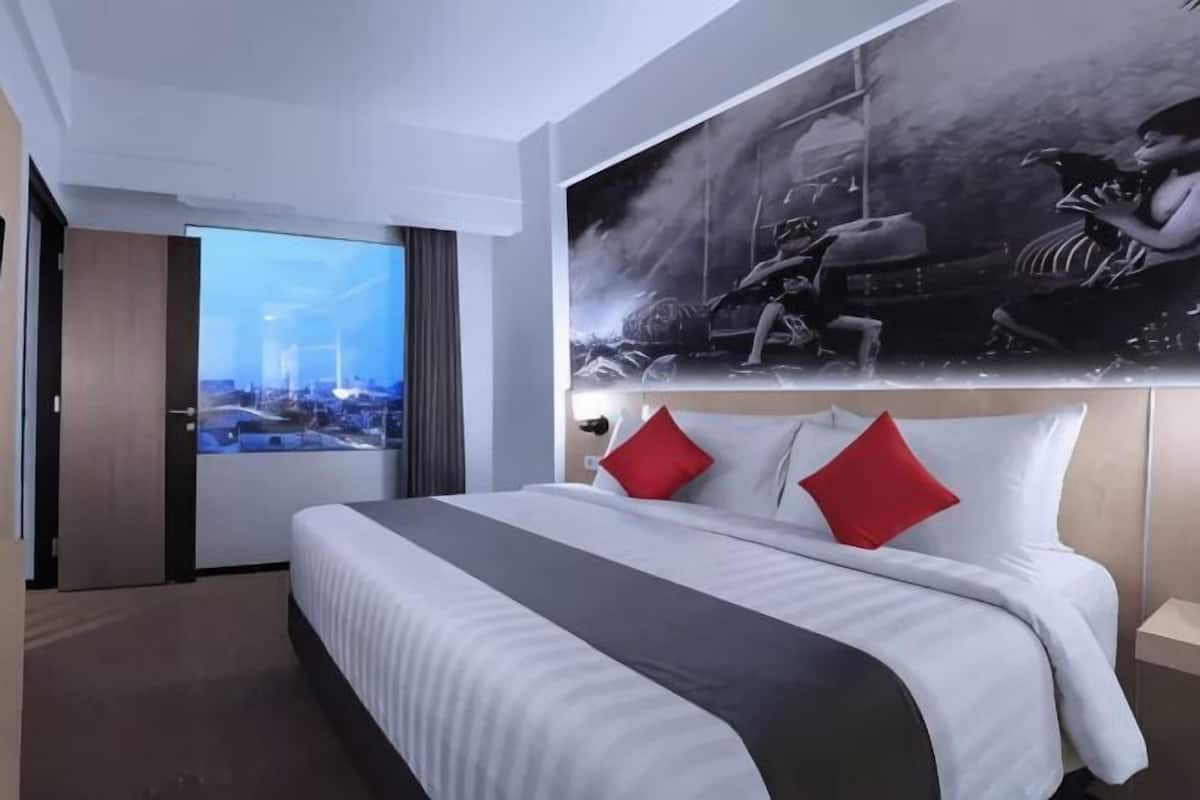 Hotellihuone, jossa on suuri sänky, liukuovesta avautuva näkymä kaupunkiin ja suuri taideteos sängyn yläpuolella.