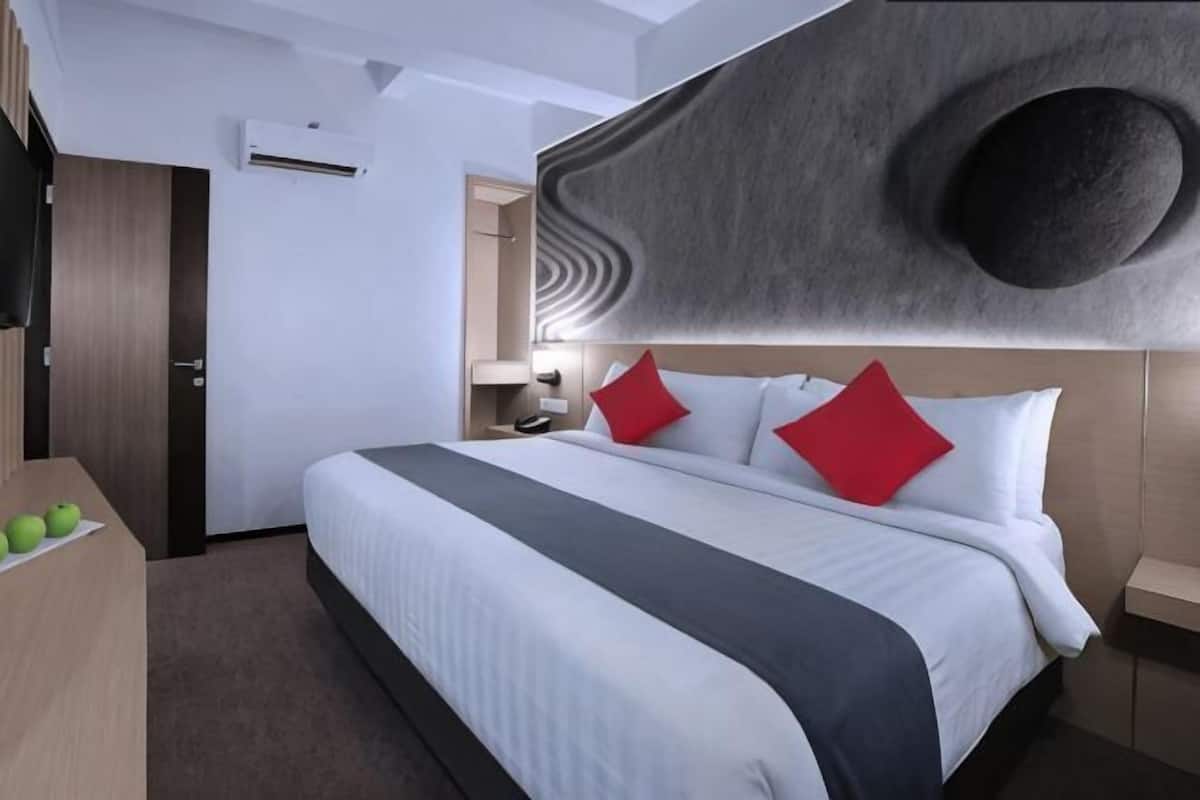 Moderni hotellihuone, jossa on suuri sänky, taulutelevisio, työpöytä, jossa on omenoita, ja ainutlaatuinen seinäkoriste.