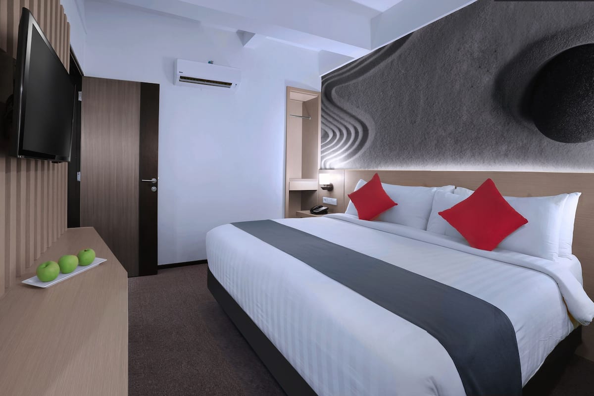 Hotellihuone, jossa on sänky, pöytä, jossa on omenoita, taulutelevisio, seinään asennettu ilmastointilaite ja ainutlaatuinen, kuvioitu seinäpinta.