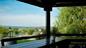 An outdoor wooden bench with a view of a rural landscape, including trees and a distant road. - Guest House Zevnik (Brezice)
