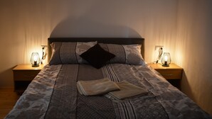 A neatly made bed with patterned bedding and pillows, flanked by two bedside tables with lamps, set against a plain wall. - Guest House Zevnik (Brezice)