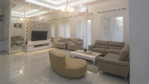 A modern living room with a flat-screen TV, beige sofas, a coffee table, and a chandelier. - Royal Homy Syariah (Depok)
