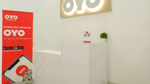 A reception area with a large OYO Hotels sign, a promotional poster, and a small plant on a white counter. - Royal Homy Syariah (Depok)