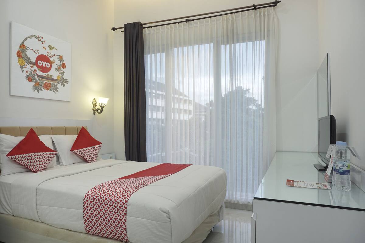 A hotel room with a bed, a TV, a glass table, a curtain, and a wall decoration.