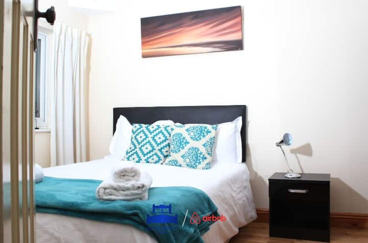 Een opgemaakt bed met gestreepte kussens, een bedlampje en een aan de muur hangend schilderij.