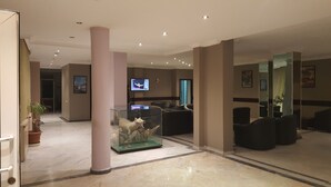 A lobby with a glass display case containing a taxidermy animal, a television mounted on the wall, and a seating area with leather chairs. - Ata Hotel Kumburgaz (Istanbul)