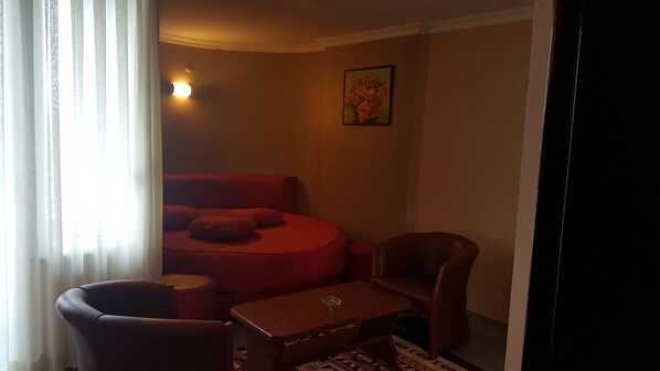 Une petite pièce à la lumière tamisée, avec un canapé rouge, une chaise en bois et une petite table.
