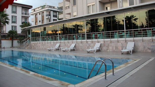 A swimming pool with lounge chairs, a glass wall, and a building with balconies. - Ata Hotel Kumburgaz (Istanbul)