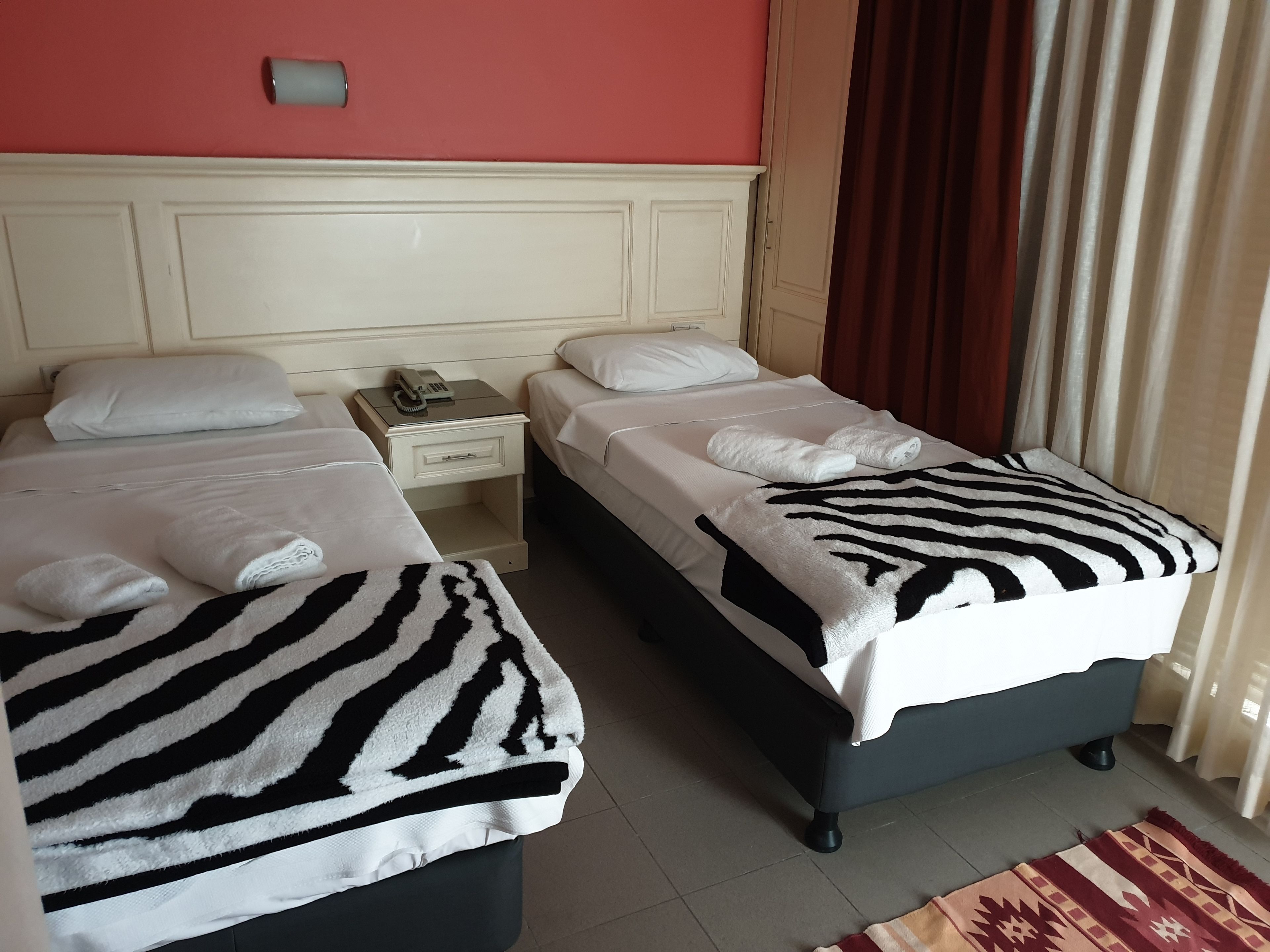 A hotel room with two beds, each with a zebra-patterned blanket and white pillows. There is a nightstand with a phone and a lamp between the beds.