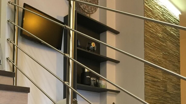 Una escalera moderna con barandillas de metal, estantes integrados y un panel decorativo en la pared.