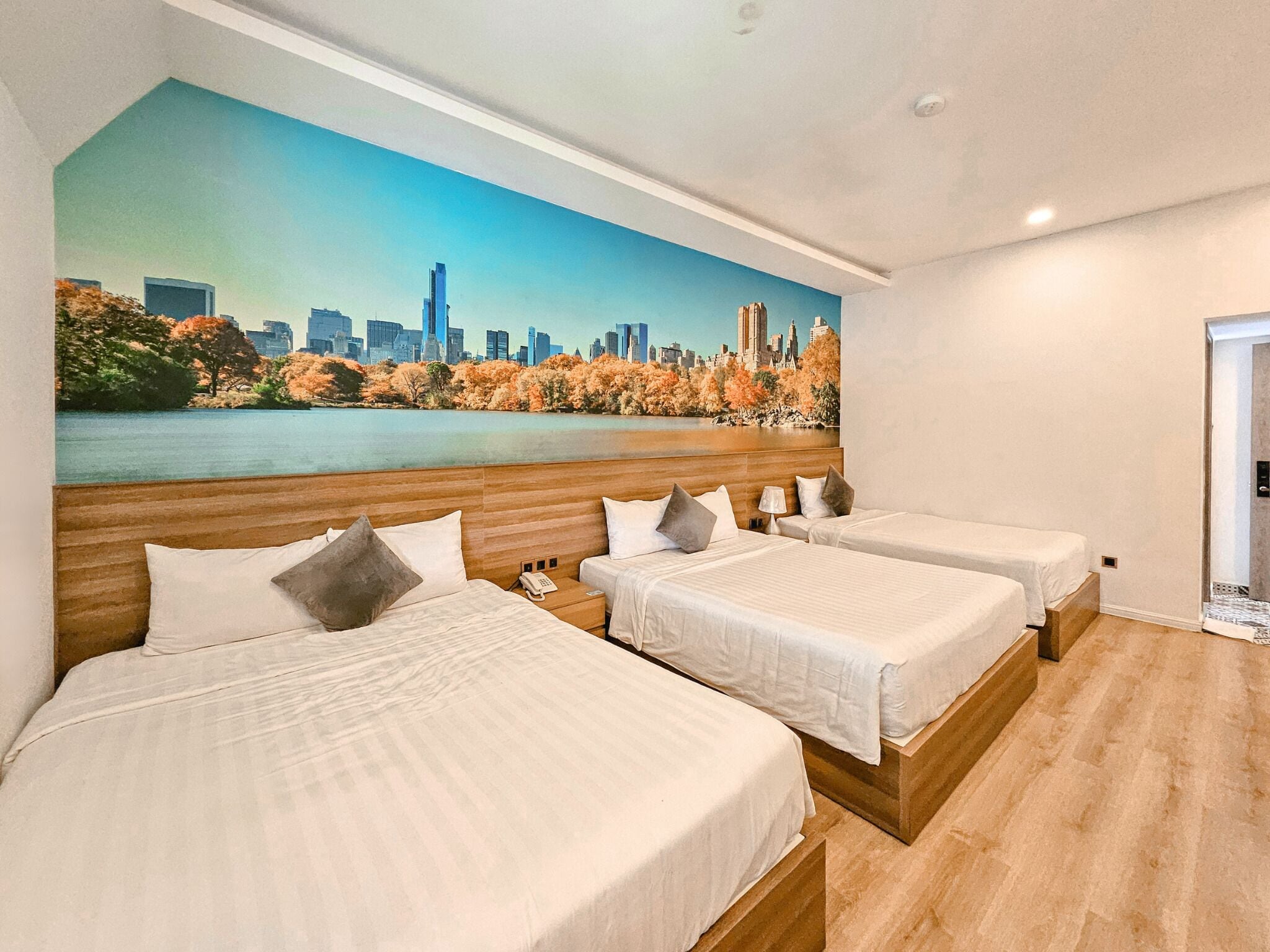 A hotel room with two beds, a cityscape mural, and a view of a lake.