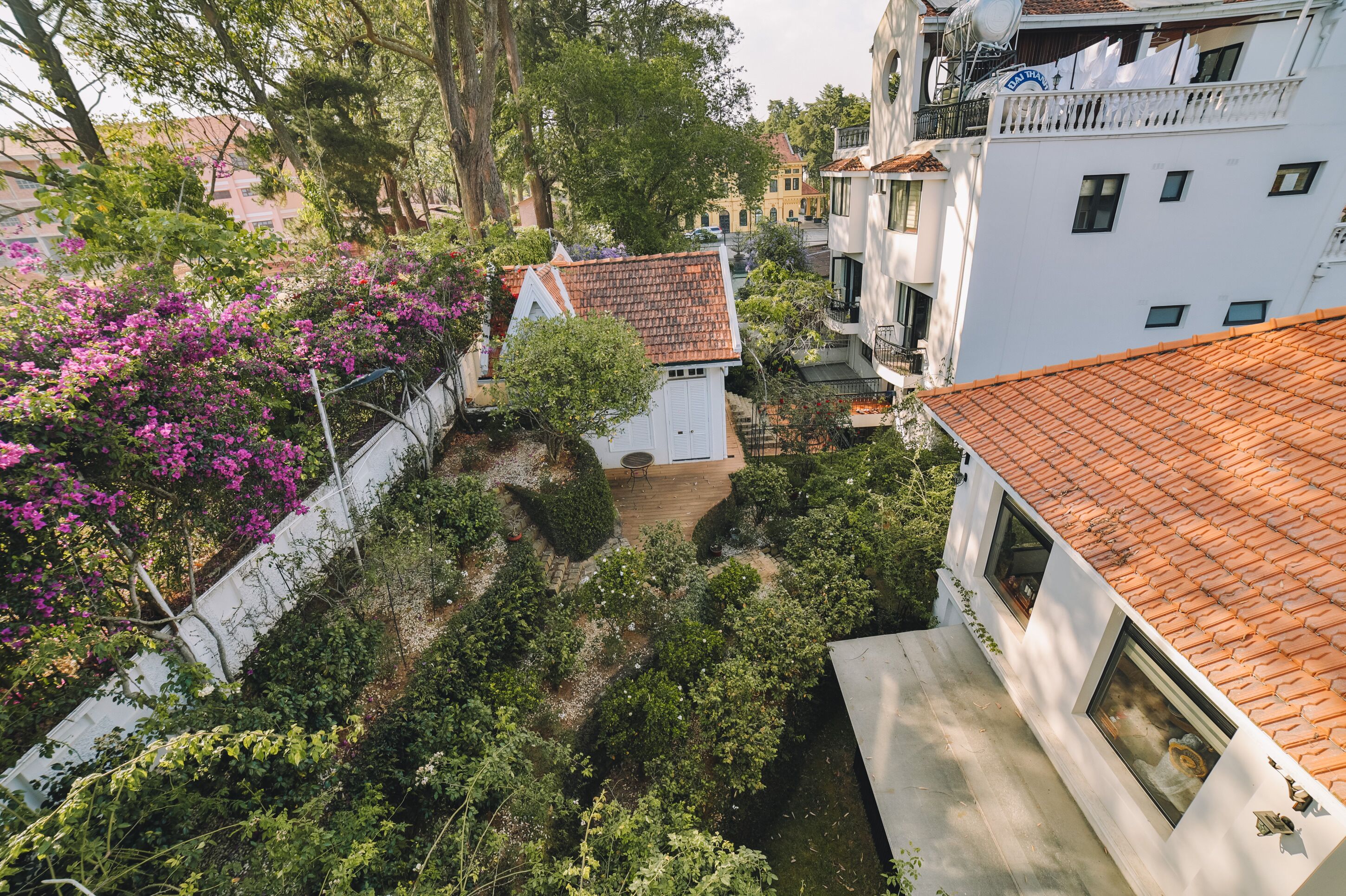 Un patio con un edificio blanco, tejado de tejas rojas y abundante vegetación.