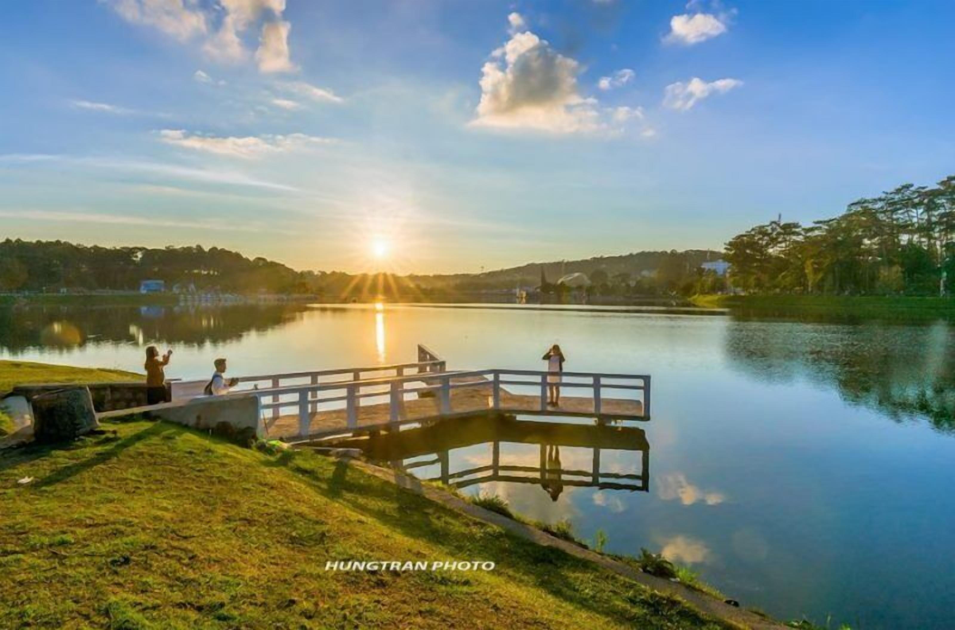 Una escena tranquil·la al costat d'un llac, amb un moll de fusta que s'endinsa a l'aigua, envoltat per vessants de gespa i arbres.