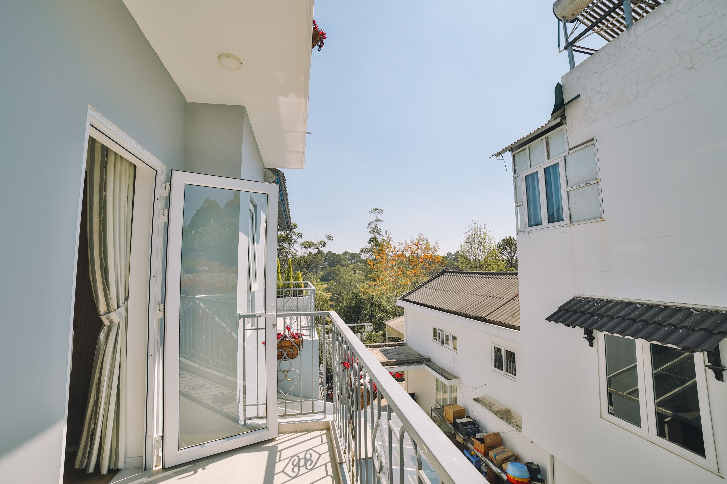 A narrow corridor between buildings with a balcony on the left, a white building on the right, and a clear sky.