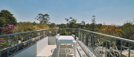 A balcony with a white table and chairs, surrounded by a metal railing and potted plants.