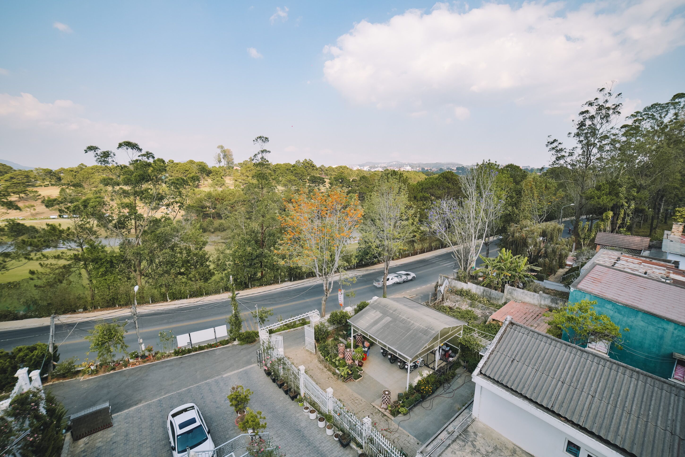 Área residencial com rua, carros estacionados e um pequeno edifício com varanda coberta.