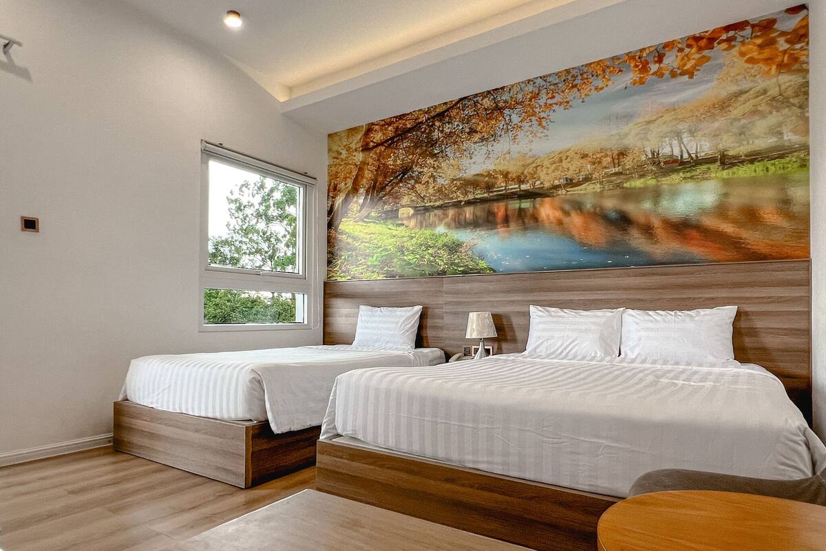 A hotel room with two beds, a large window, and a painting of a landscape.